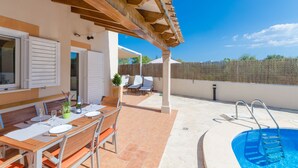 Un espace extérieur abrité comprenant une piscine, une table à manger pour quatre personnes et une terrasse avec des chaises et une petite table.