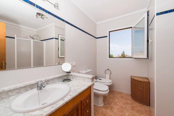 A bathroom with a white sink, a mirror, a toilet, and a window.