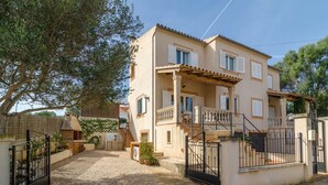 Une maison à deux étages avec une allée pavée, une entrée fermée par un portail et un petit jardin agrémenté de plantes en pot.