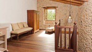 A rustic room with a wooden floor, a stone wall, a wooden wardrobe, a bench, a small table, and a window with a view of greenery. - CAN GUILLO - Villa with private pool in Pollensa. Free WiFi (Pollensa / Pollença)