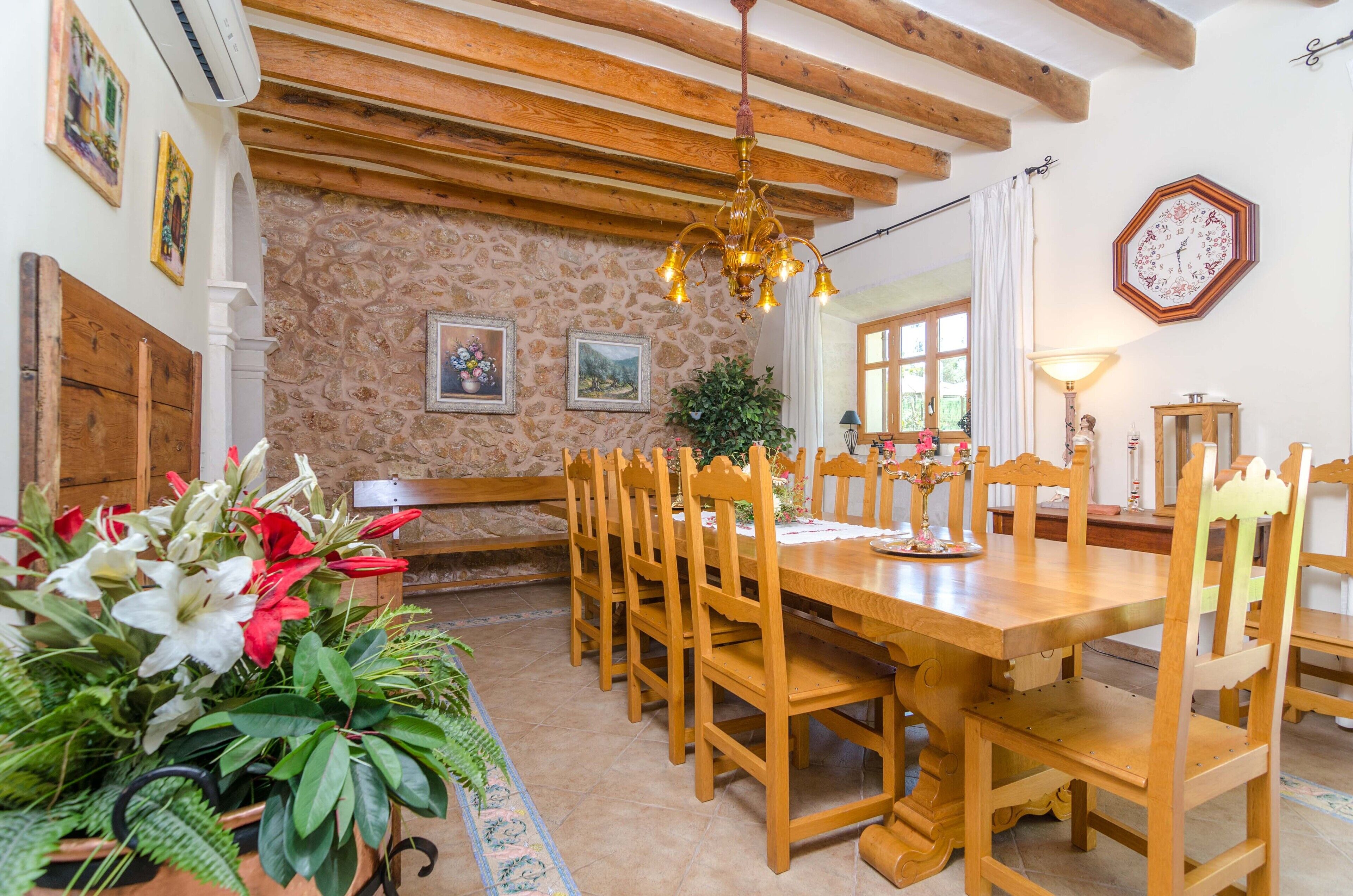 A dining area with a wooden table and chairs, a chandelier, and a stone wall with framed pictures.