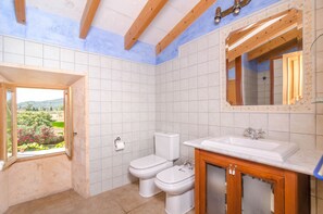 A bathroom with white tiles, a wooden vanity, a sink, and a window with a view of greenery.