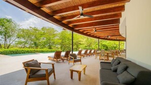 An outdoor seating area with wooden furniture and ceiling fans, overlooking a lush green landscape.