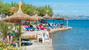 Un complexe hôtelier en bord de mer, doté de parasols en chaume, de chaises longues et offrant une vue dégagée sur la mer.
