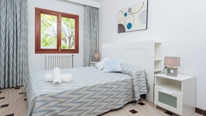 Une chambre d’hôtel avec un lit, une table de chevet, une lampe, un tableau et une fenêtre avec des rideaux.