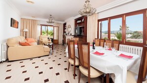 Un coin repas avec une table dressée pour deux personnes, un canapé et un téléviseur en arrière-plan.