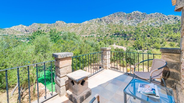 A balcony with a stone bench, a wicker chair, and a glass table with a magazine. - SA TARONGERA - Villa with private pool in ANDRATX. Free WiFi (Andratx)