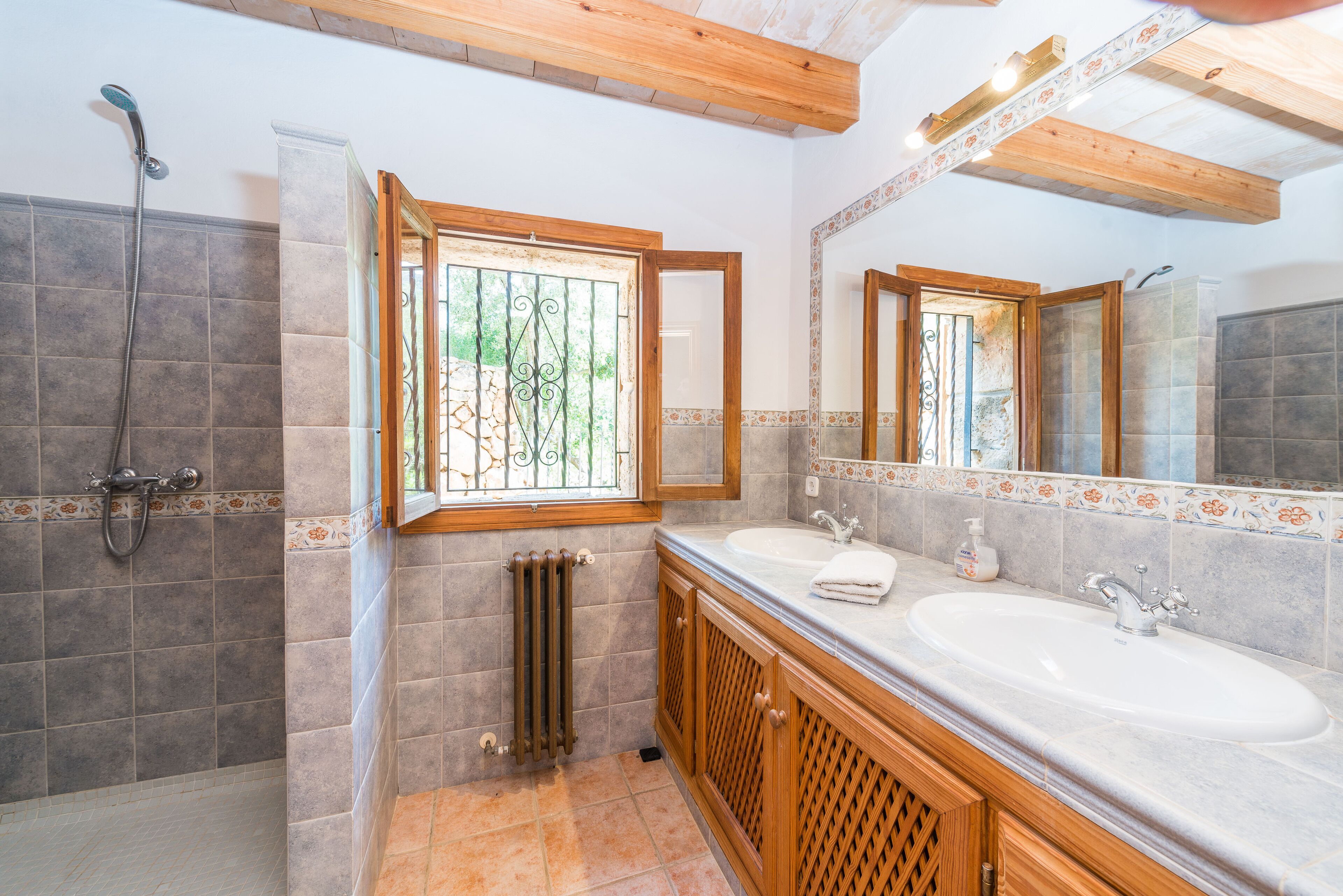 Baño con dos lavamanos, ducha y ventana con barandillas decorativas.