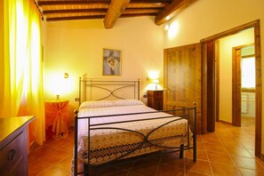 A bedroom with a metal bed frame, a bedside table with a lamp, and a door leading to another room.