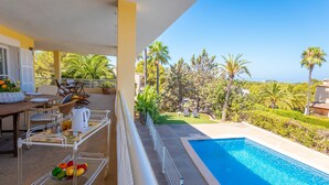 Área na beira da piscina com uma mesa, cadeiras e um carrinho de metal com frutas.