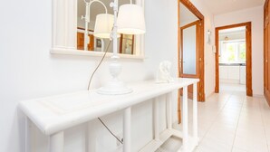 Um corredor com um console branco, um espelho e um abajur.