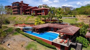 Un edificio grande de varios pisos con piscina, asientos exteriores y un jardín ajardinado.