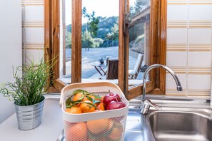 Eine Küche mit Spüle, einem Fenster mit Holzrahmen, einem Blumentopf und einem Obstkorb.