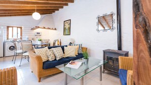A cozy living room with a sofa, a glass coffee table, a wicker chair, a fireplace, and a kitchen area in the background. - CAN CAPET - Villa with private pool in Andratx. Free WiFi (Andratx)