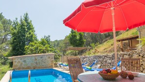 A poolside area with a stone wall, lounge chairs, and a table with a fruit basket. - CAN CAPET - Villa with private pool in Andratx. Free WiFi (Andratx)