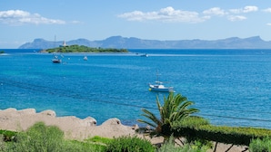 Vista costera con barcos en el agua, un faro y montañas al fondo.