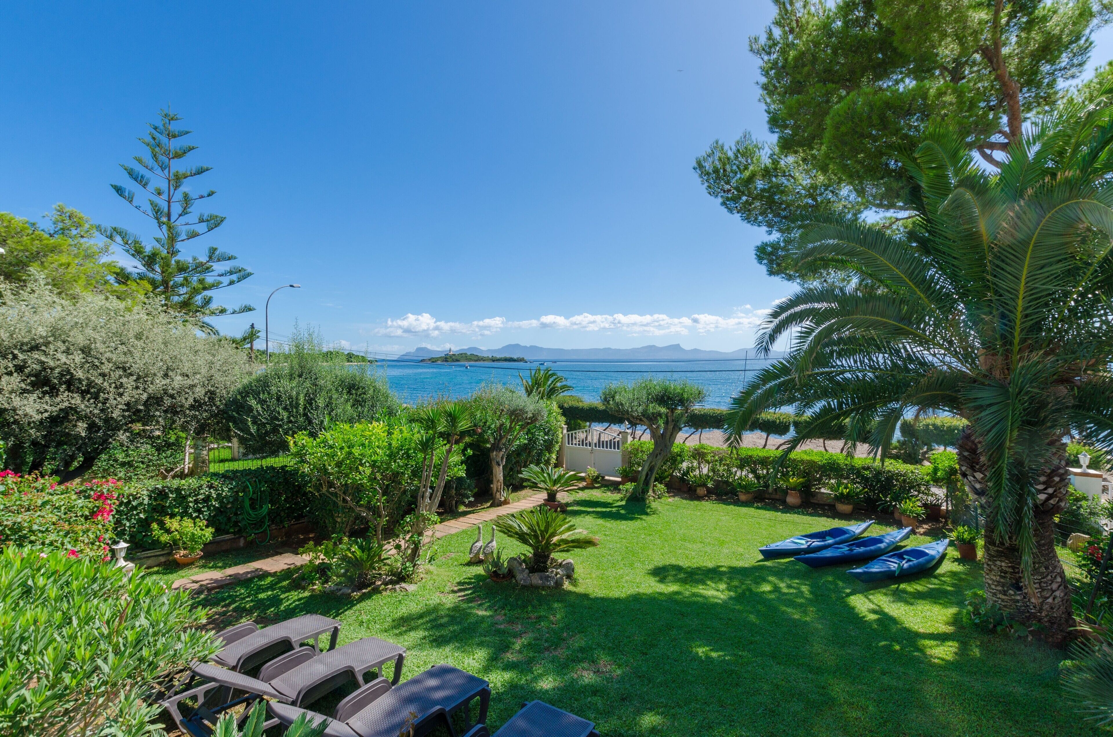 A garden with a view of the sea, a pathway, and blue lounge chairs.