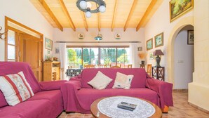 Ein Wohnzimmer mit Holzboden, einem pinken Sofa, einem runden Holztisch und Blick ins Freie durch große Fenster.
