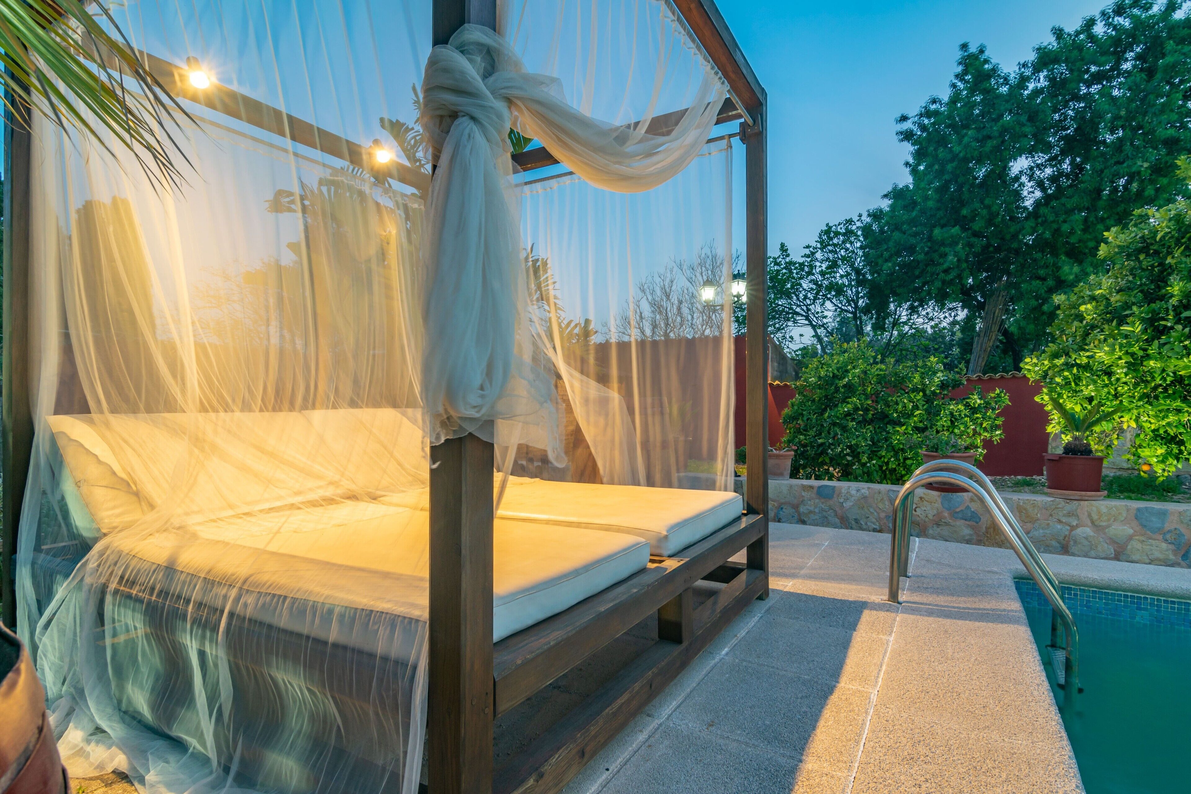 A bed with a canopy in an outdoor setting near a pool.