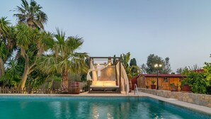Ein Poolbereich mit Holzterrasse, überdachter Sitzgelegenheit und einer Steinwand.