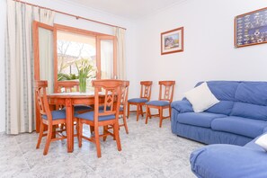 A dining area with a wooden table and chairs, a blue sofa, and a window with curtains.