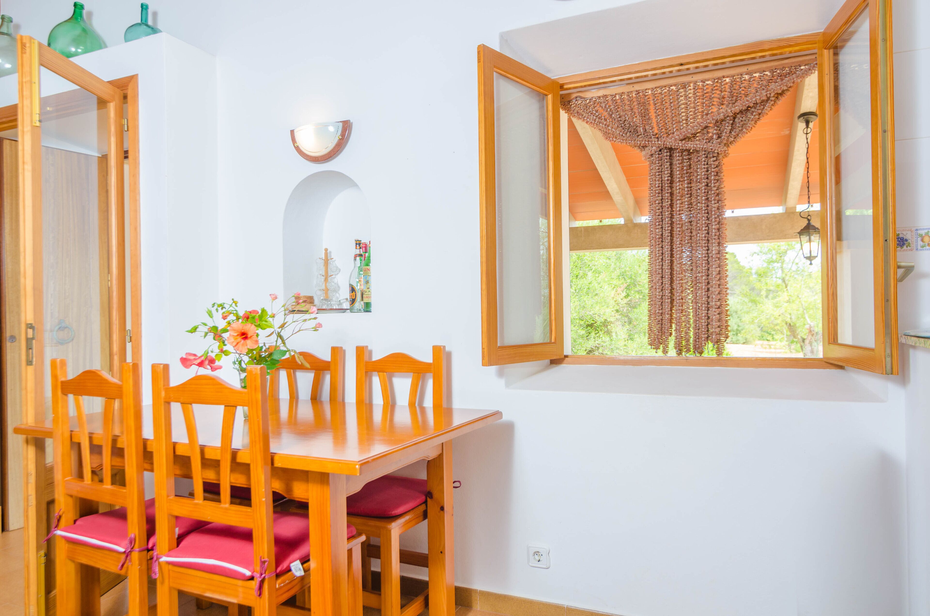 A dining area with a wooden table and chairs, a window with a woven curtain, and a wall-mounted light fixture.