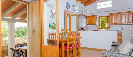 A spacious living area with a dining table and chairs, a sofa, and a kitchen with wooden cabinets and a window.