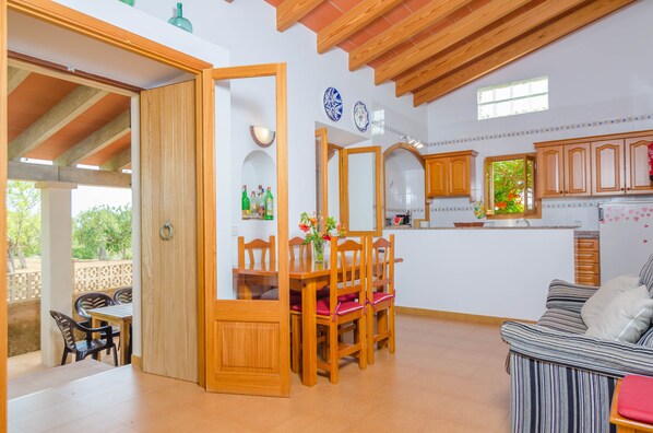 A spacious living area with a dining table and chairs, a sofa, and a kitchen with wooden cabinets and a window.