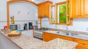 Una cocina con encimeras de granito, armarios de madera, horno empotrado, pileta y ventana con vista a follaje.