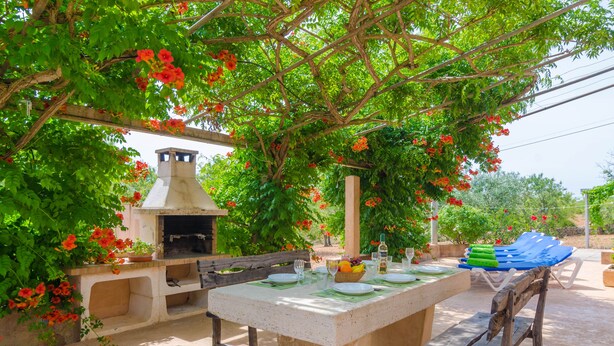Un área de comedor al aire libre con una mesa de piedra, bancos y una parrilla.