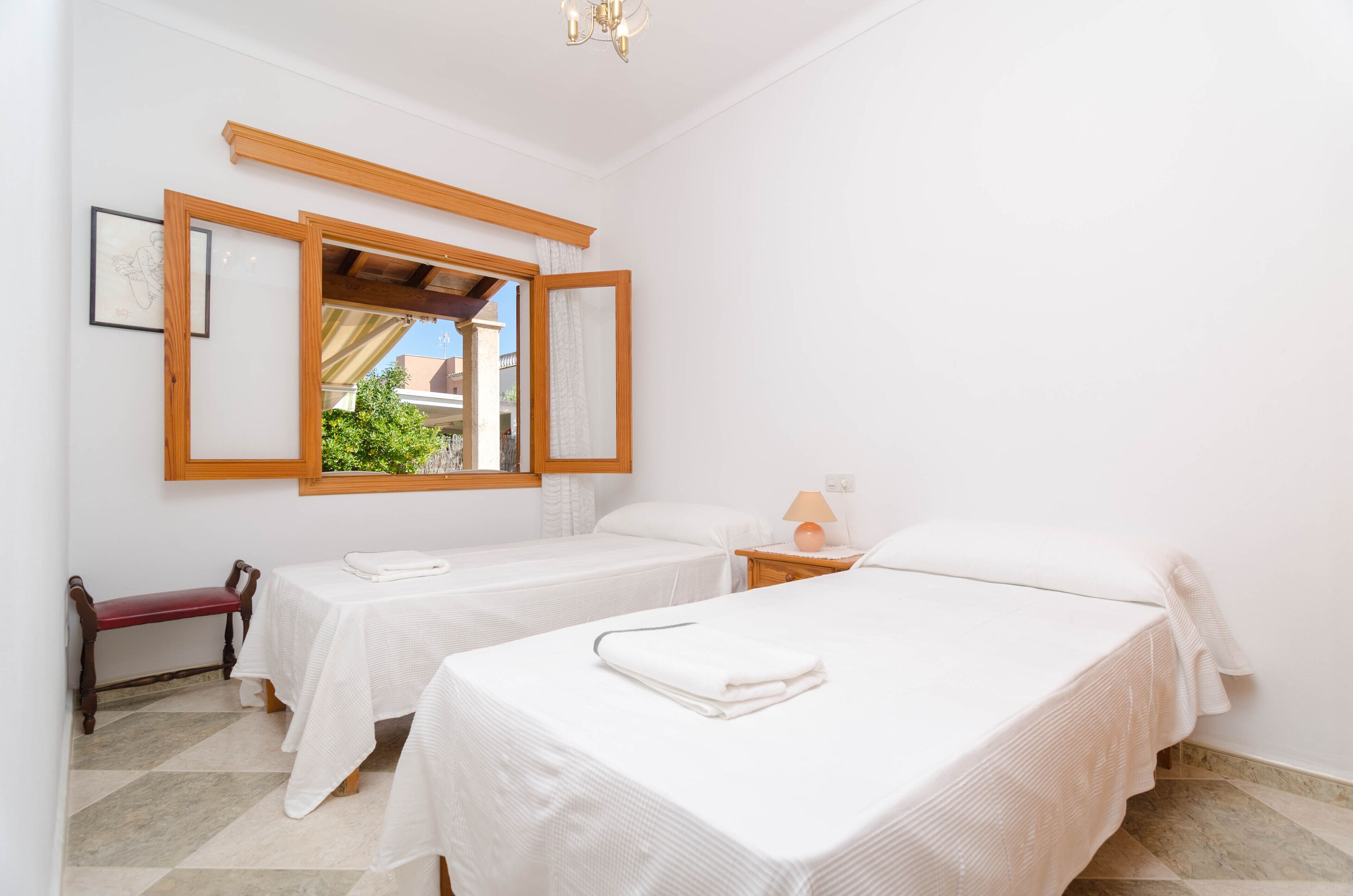 Ein Hotelzimmer mit zwei Betten, einer Bank, einem kleinen Tisch und einem Fenster mit Blick auf Grün.