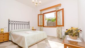 A bedroom with a bed, bedside tables, a nightstand, a window with curtains, a chandelier, and a small table with a vase of flowers. - ES PORT  - Beautiful holiday home with private garden in Portocolom. Free WiFi (Portocolom)