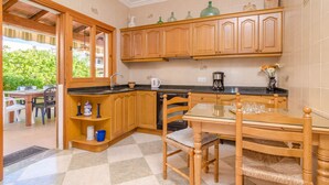 A kitchen with wooden cabinets, a dishwasher, and a dining area with a table and chairs. - ES PORT  - Beautiful holiday home with private garden in Portocolom. Free WiFi (Portocolom)