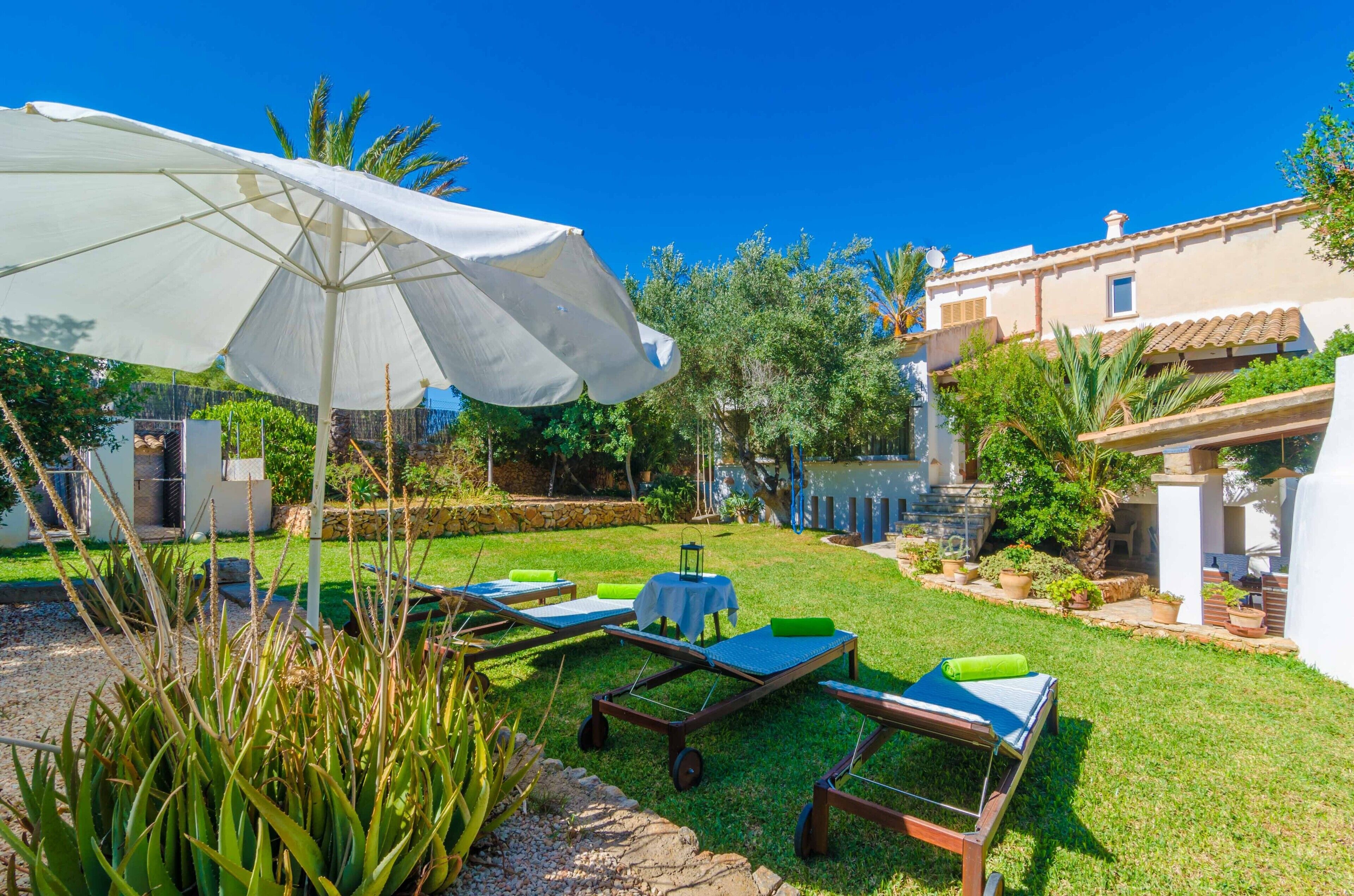 Une terrasse ensoleillée, aménagée à l’extérieur, avec des chaises longues, un grand parasol et une petite table.