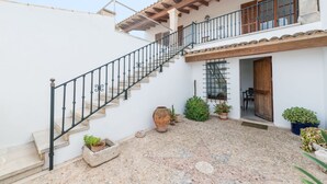 Eine Treppe führt zu einem zweiten Stock mit einem hölzernen Balkon, Blumentöpfen und einer rustikalen Steinwand.