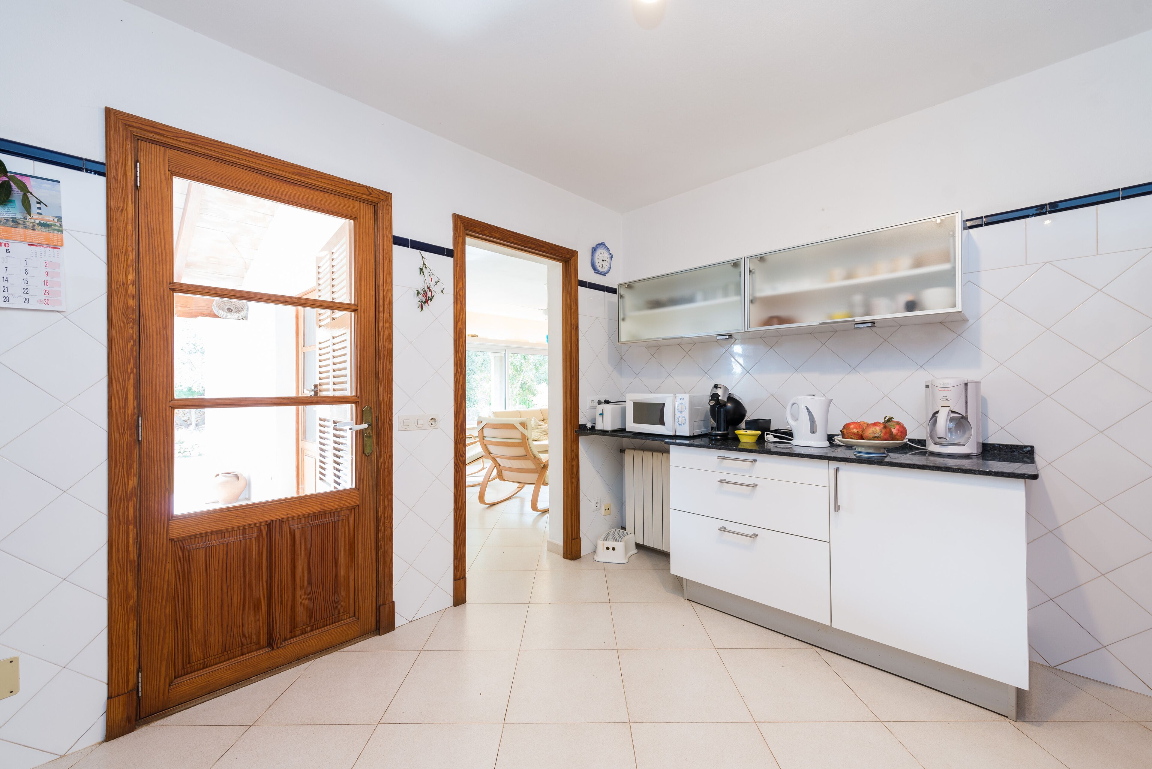 A kitchen with white cabinets, a microwave, and a kettle on the counter.