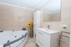 A modern bathroom with a large bathtub, a white vanity, a mirror, and a vase with sunflowers.