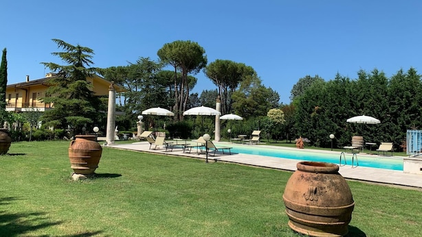 A pool area with lounge chairs and umbrellas, surrounded by greenery and a building in the background.