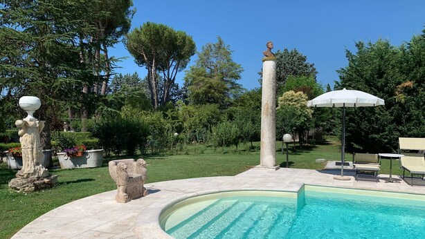 Una piscina con una fuente de piedra, rodeada por un jardín con diversas plantas y árboles.