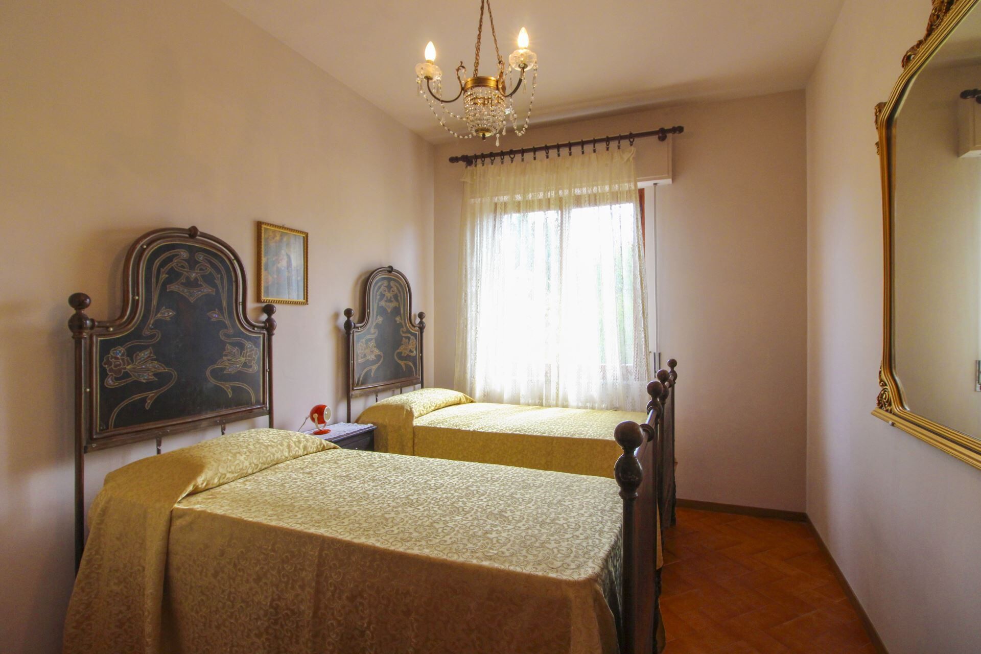 Une chambre avec deux lits, un lustre, un miroir et une fenêtre avec des rideaux.