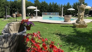 A swimming pool with lounge chairs and umbrellas, surrounded by greenery and a statue.