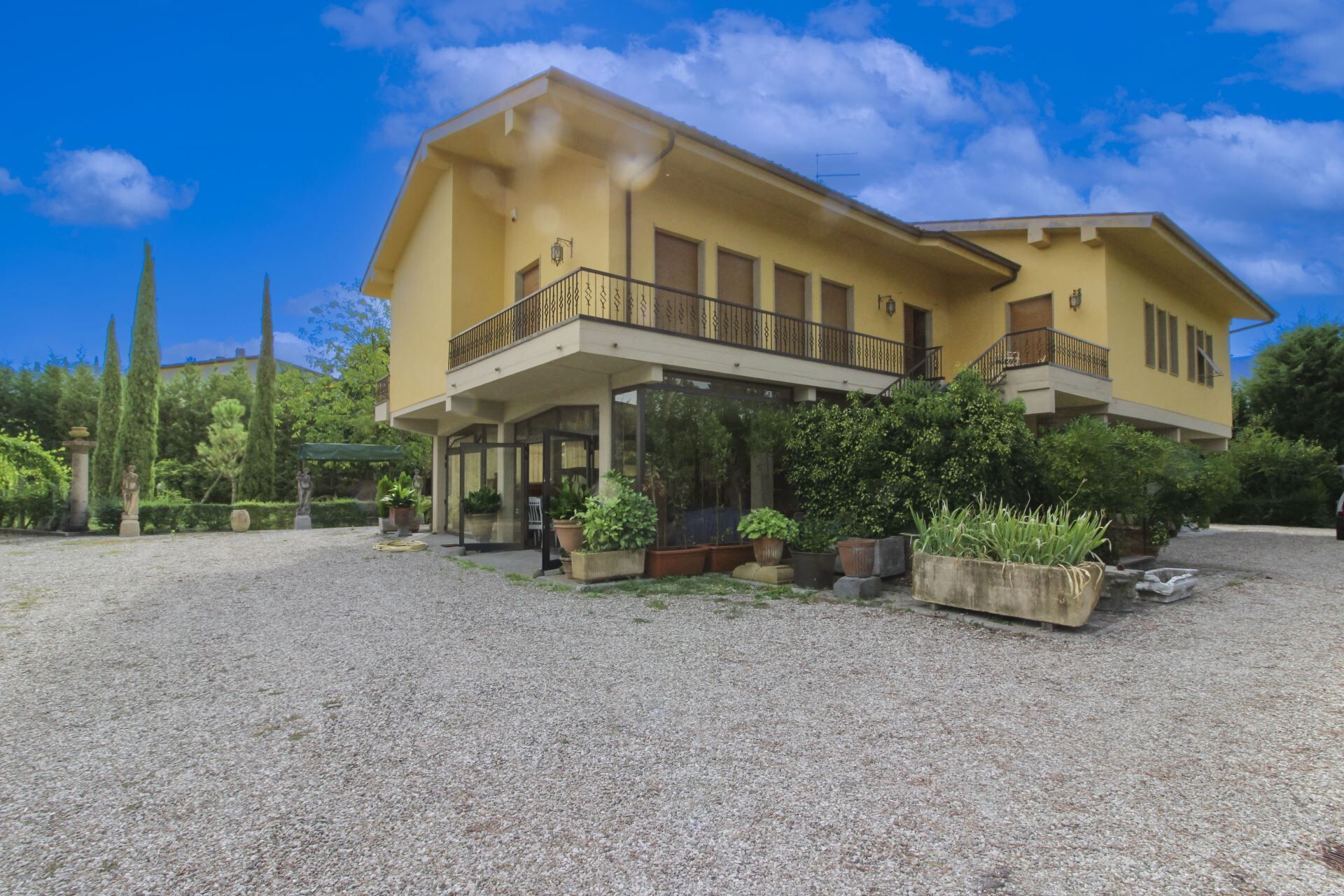 A two-story building with a balcony, surrounded by gravel and greenery.