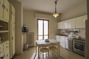 A kitchen with a dining table, chairs, a coffee maker, a stove, and cabinets.