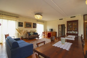 A spacious living room with a wooden dining table, sofas, and a television.