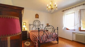 A bedroom with a bed, a nightstand, a dresser, a chandelier, and a window with curtains.