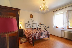 A bedroom with a bed, a nightstand, a dresser, a chandelier, and a window with curtains.