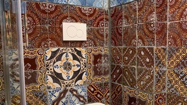 Une salle de bain avec des toilettes blanches, des carreaux décorés et une douche en verre.