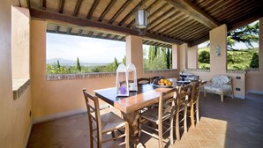 An outdoor patio with a wooden table and chairs, a lantern, and a view of the landscape.