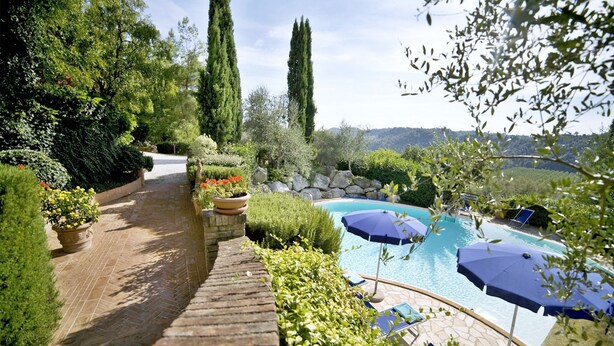 A pool area with lounge chairs and umbrellas, surrounded by lush greenery and a stone pathway.