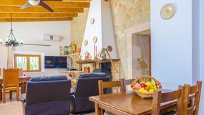 Un coin repas chaleureux avec un mur en pierre, des meubles en bois et un panier de fruits posé sur la table.